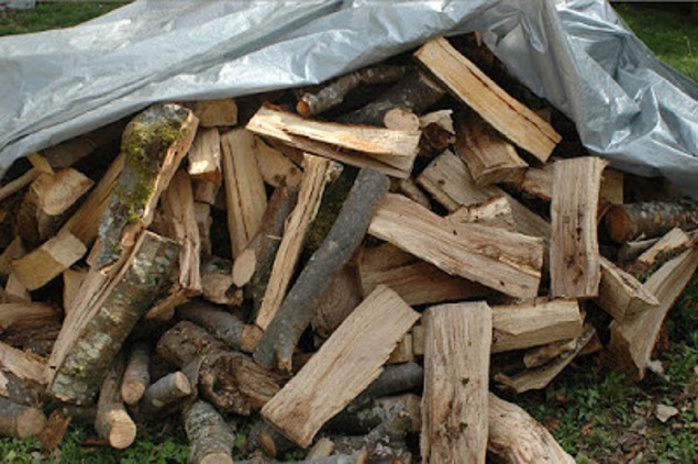 A pile of fire wood on the ground covered in a tarp